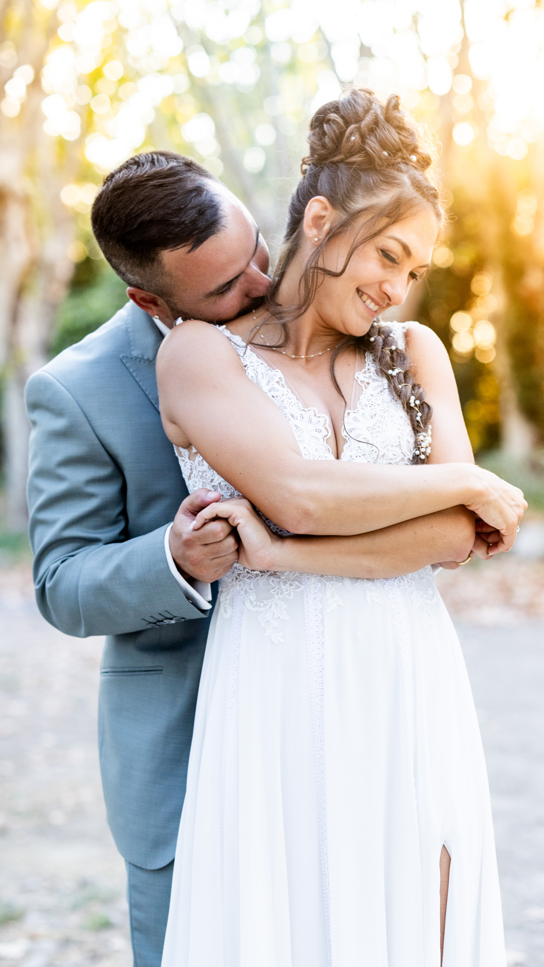 Le marié enlace tendrement sa femme et l’embrasse dans le cou, lumière dorée traversant les arbres Domaine de Sulauze